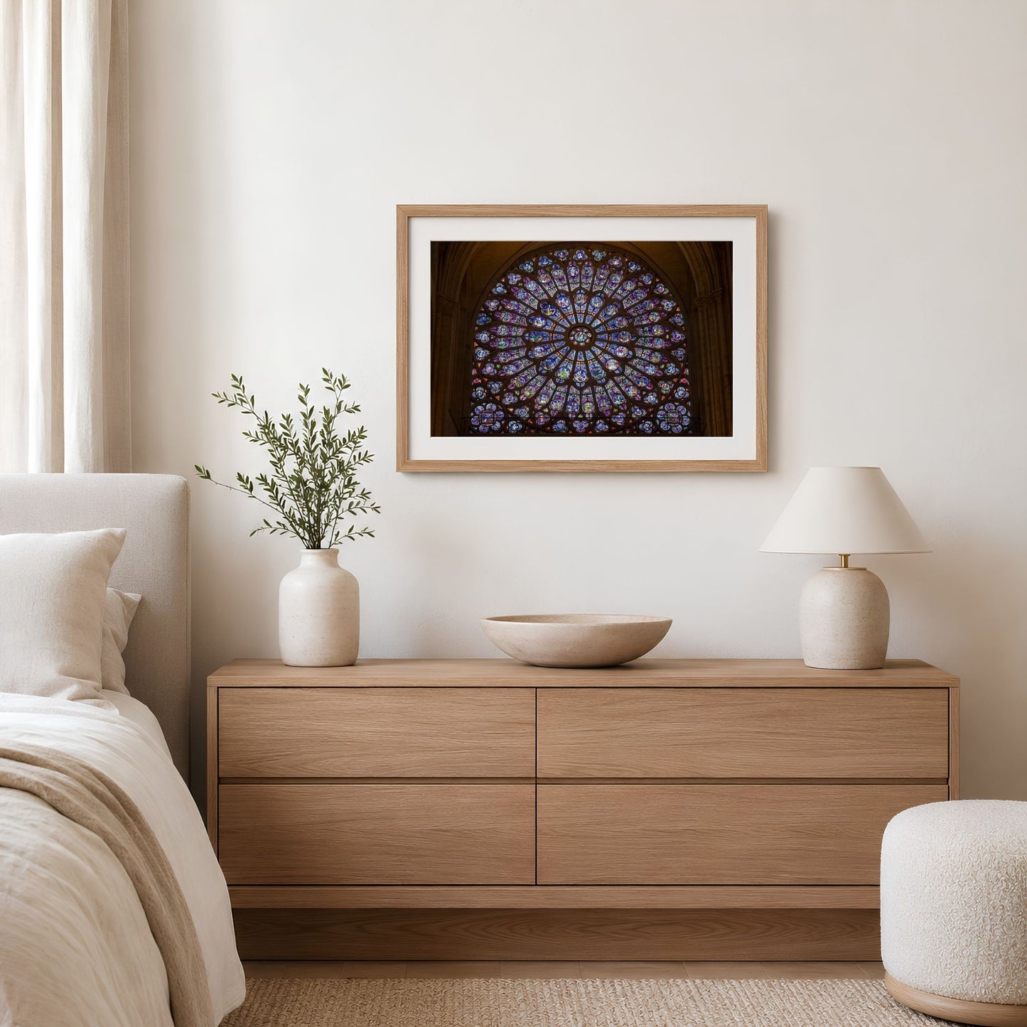 Framed Notre-Dame rose window photography print displayed above a wood dresser in a bright neutral bedroom