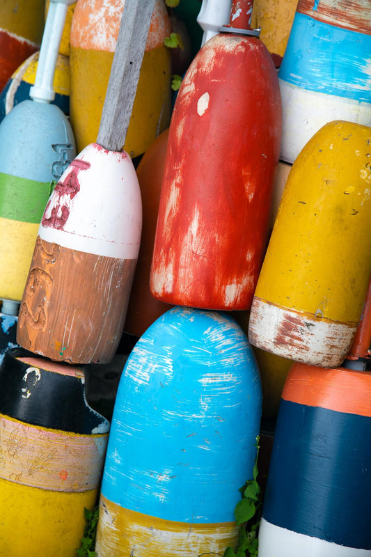 Colorful lobster buoys stacked together in Rockport, Massachusetts, with chipped red, yellow, turquoise, blue, orange, and white fishing floats photographed by Linda Nee as New England coastal nautical wall art.