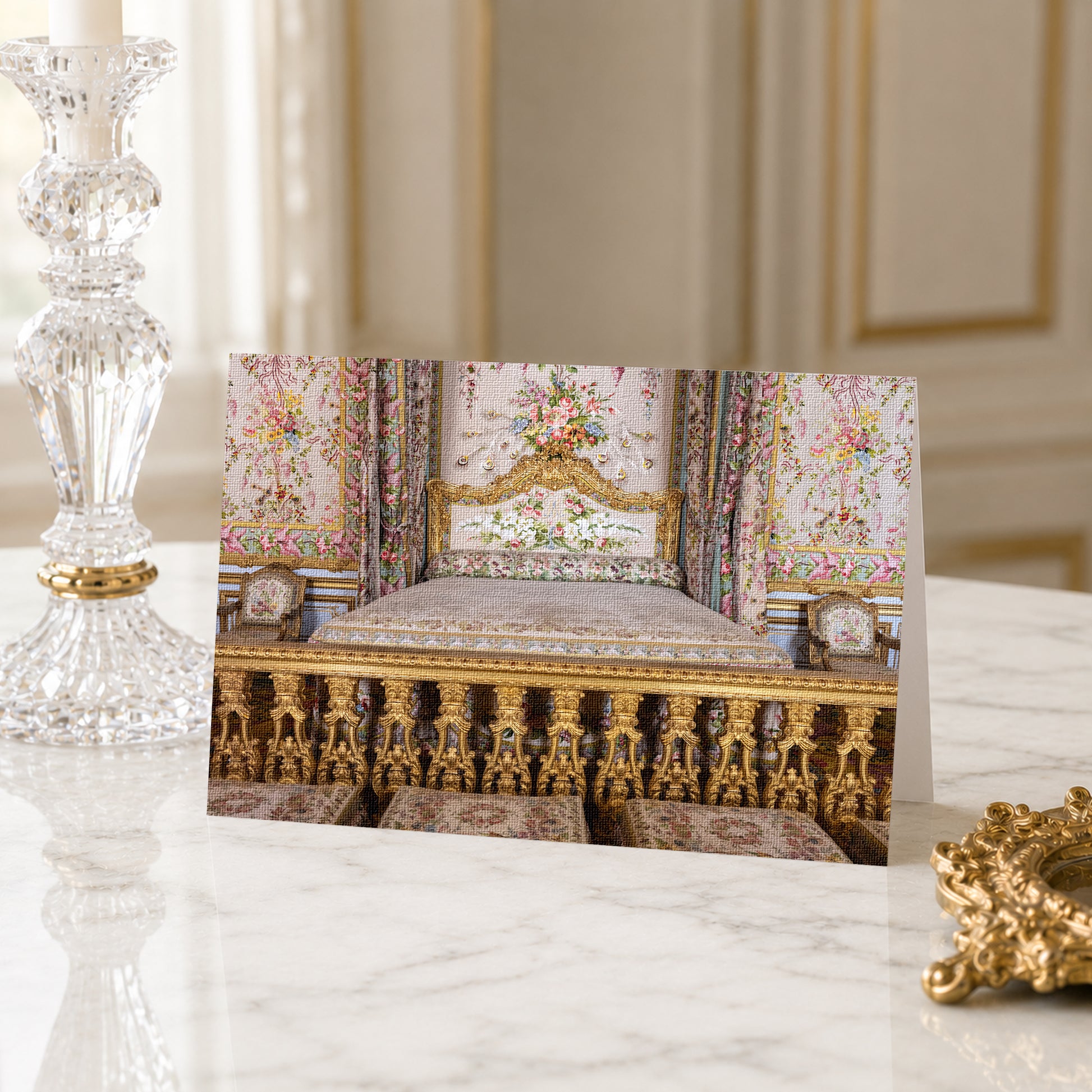 A card featuring an ornate, gold-colored bed with floral patterns, placed on a marble surface next to a crystal candlestick.