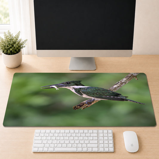 Kingfisher perched on a branch holding a small fish in its beak against a blurred green background, shown as a desk mat design on a wood desk