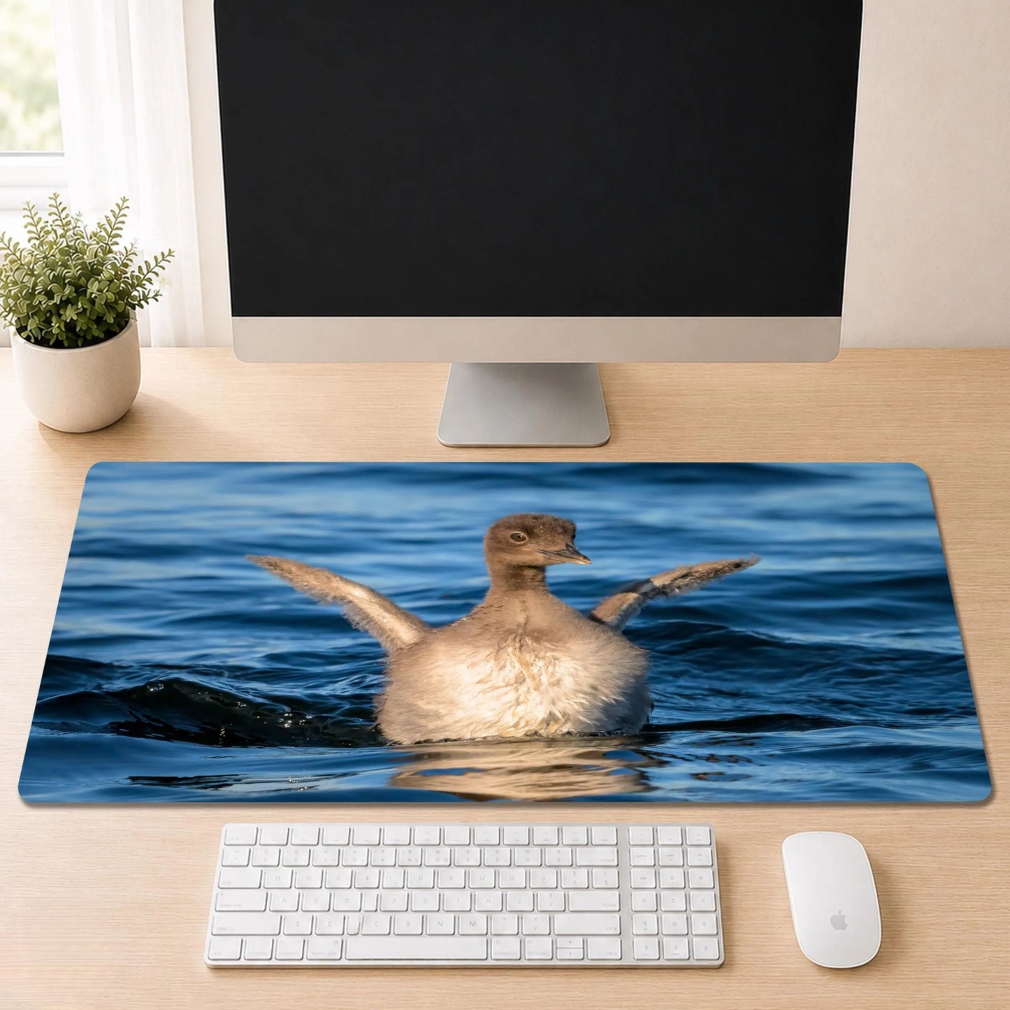 Baby Common Loon desk mat featuring original New Hampshire wildlife photography by Linda Nee, shown beneath a white keyboard on a light wood desk.