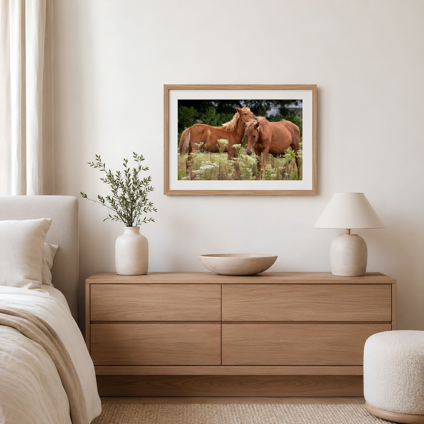 a bedroom with a wooden dresser, a framed picture of two horses, a lamp, and a plant.