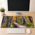 a computer desk with a monitor, keyboard, and mouse. The monitor displays a scenic image of a forest path with a wooden walkway.