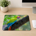 Great Green Macaw with red forehead, green body, and blue tail feathers perched on a mossy branch, printed on a mouse pad