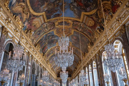 Palace of Versailles Hall of Mirrors interior with crystal chandeliers, gilded trim, painted ceiling murals, arched windows, and ornate French Baroque architecture.