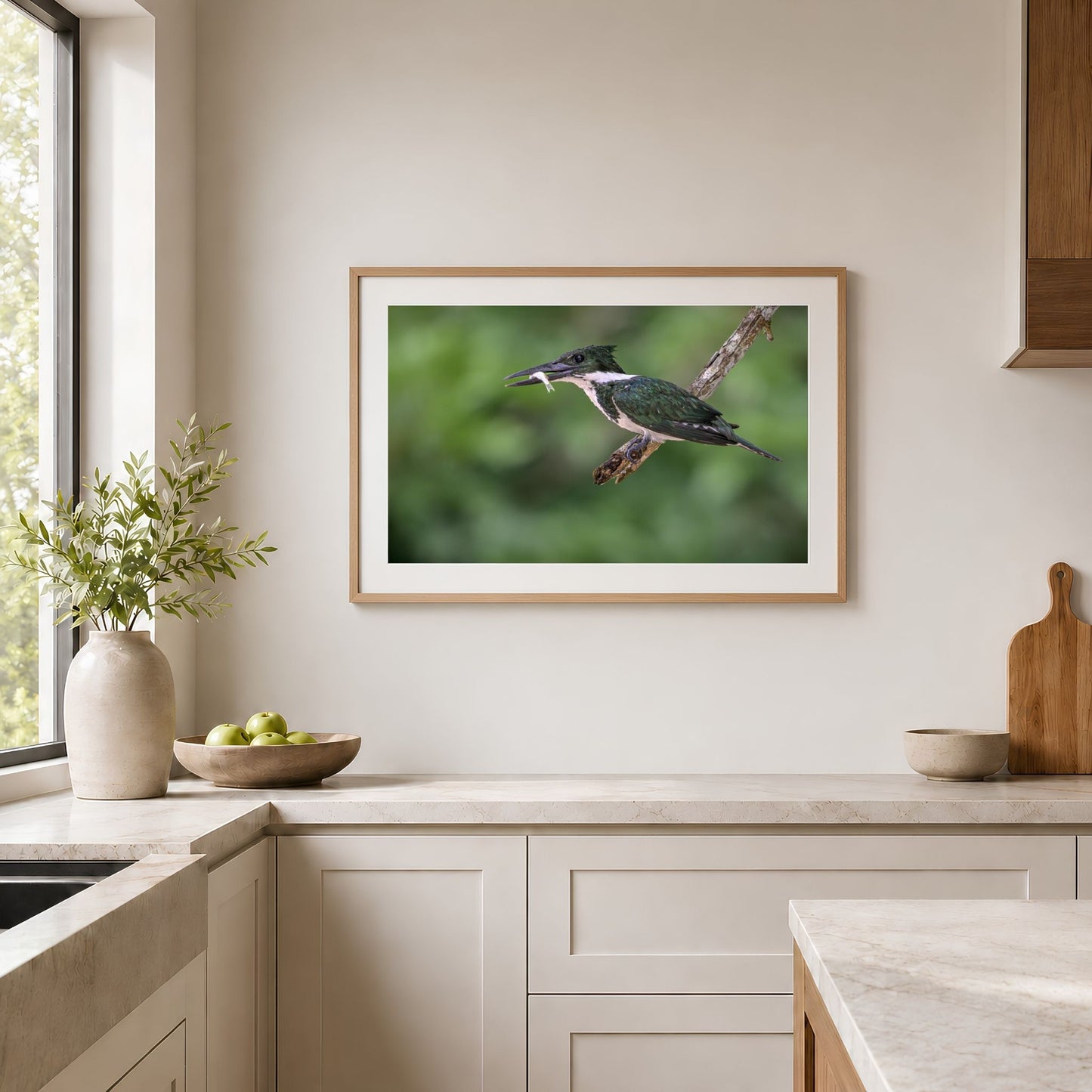 Framed landscape Amazon kingfisher photography print in a natural wood frame with white mat, displayed in a bright modern kitchen above a neutral countertop