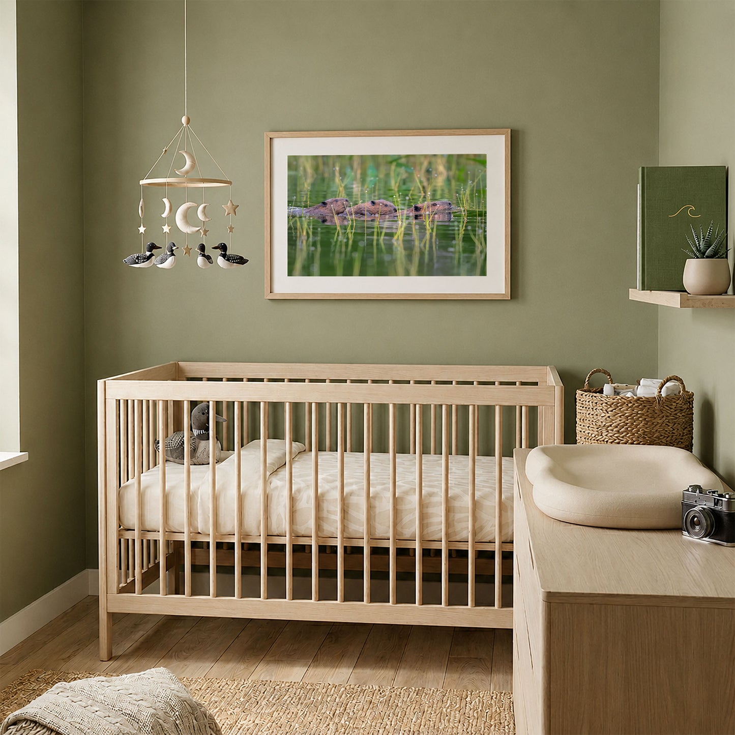 Framed beaver family photography print displayed above a natural wood crib in a cozy sage green nursery.