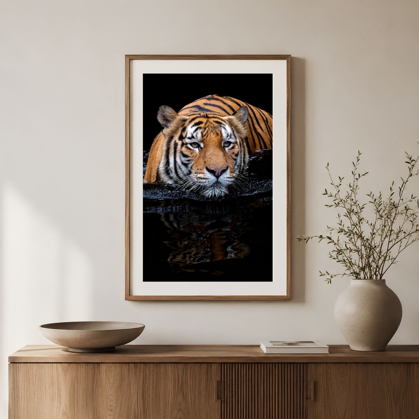 Framed vertical Bengal tiger photography print in a natural wood frame with white mat, displayed above a wooden console with neutral decor and a ceramic vase
