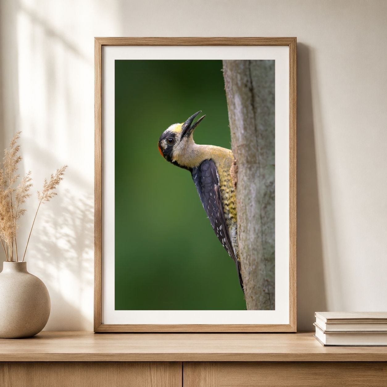 Framed picture of a bird on a branch on a wooden shelf.
