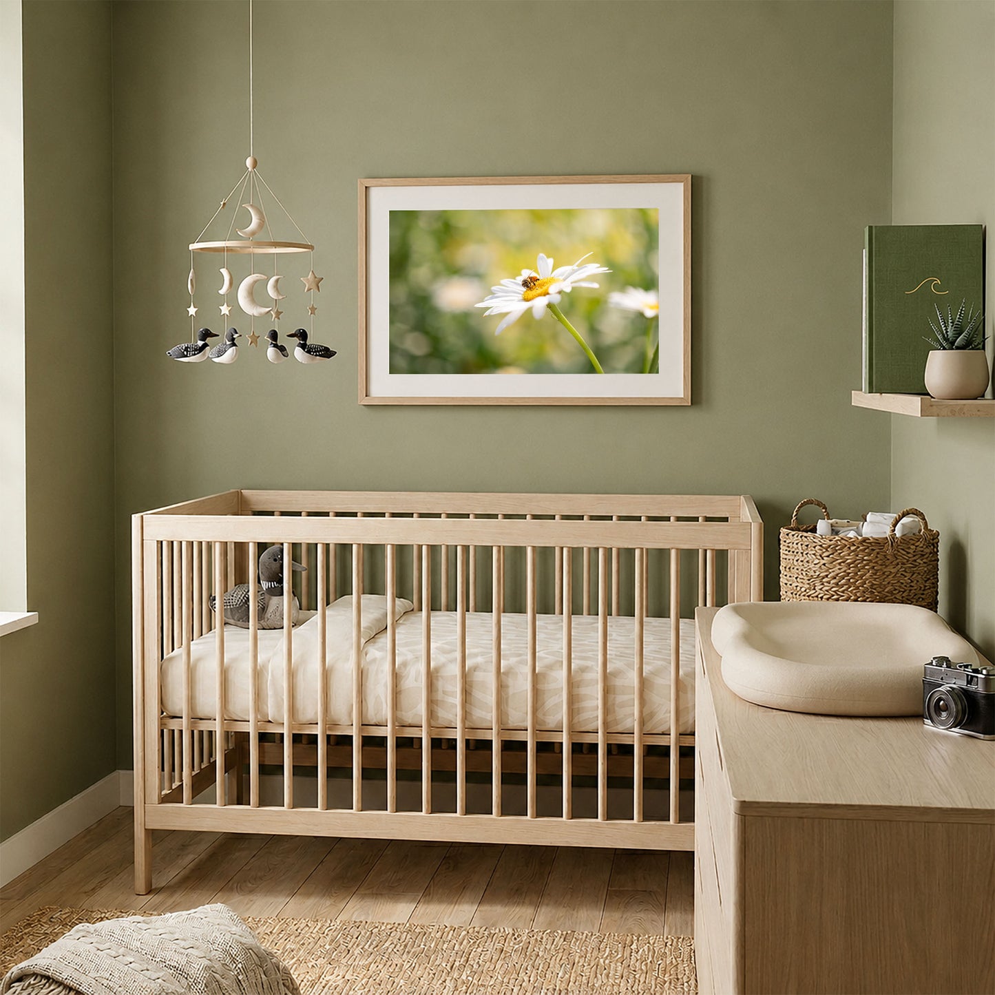 Framed honeybee on daisy photography print in a natural wood frame, displayed above a light wood crib in a soft green nursery with neutral decor