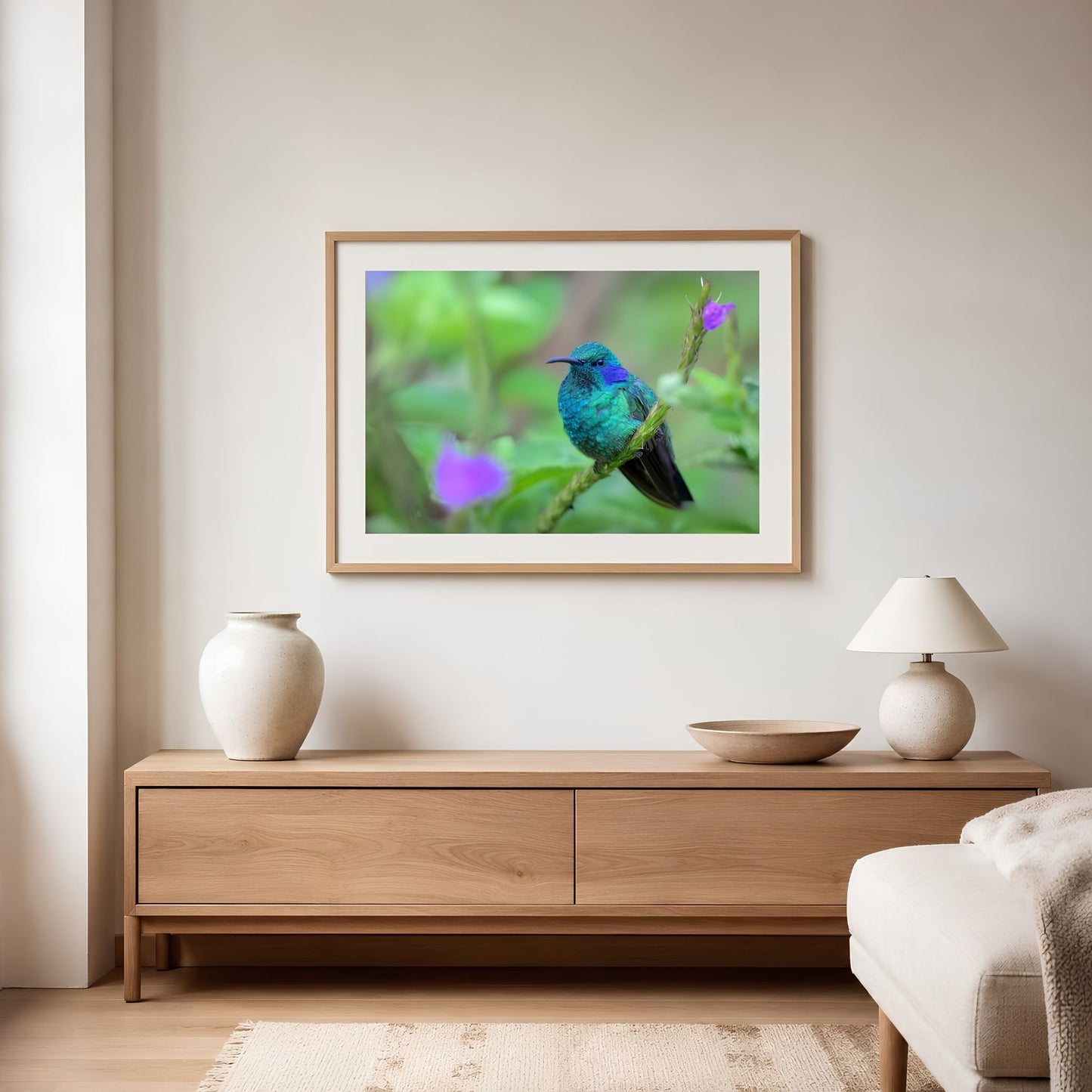 Lesser violetear hummingbird photograph in a natural wood frame, styled as landscape bird wall art for a soft modern bedroom interior.