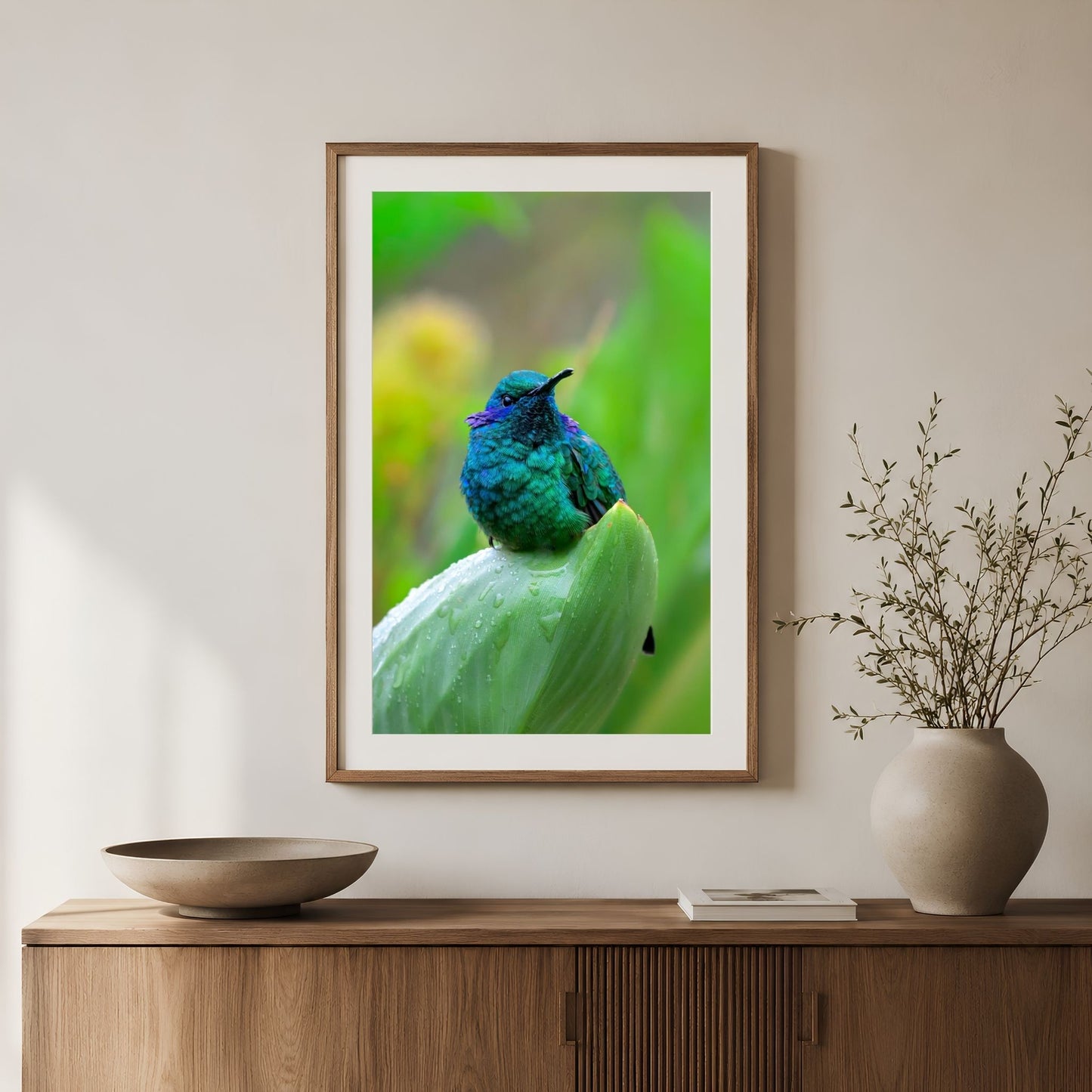 Framed artwork of a blue and green bird on a white wall above a wooden cabinet.