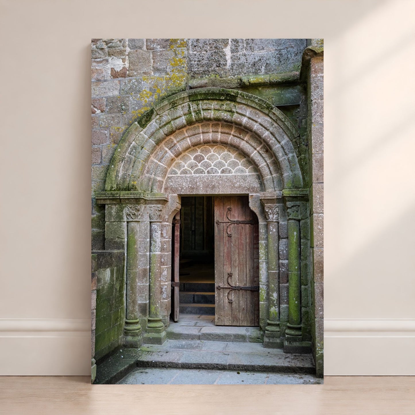 Mont Saint-Michel Abbey doorway photography print leaning against a wall, featuring an ancient stone arch and wooden door