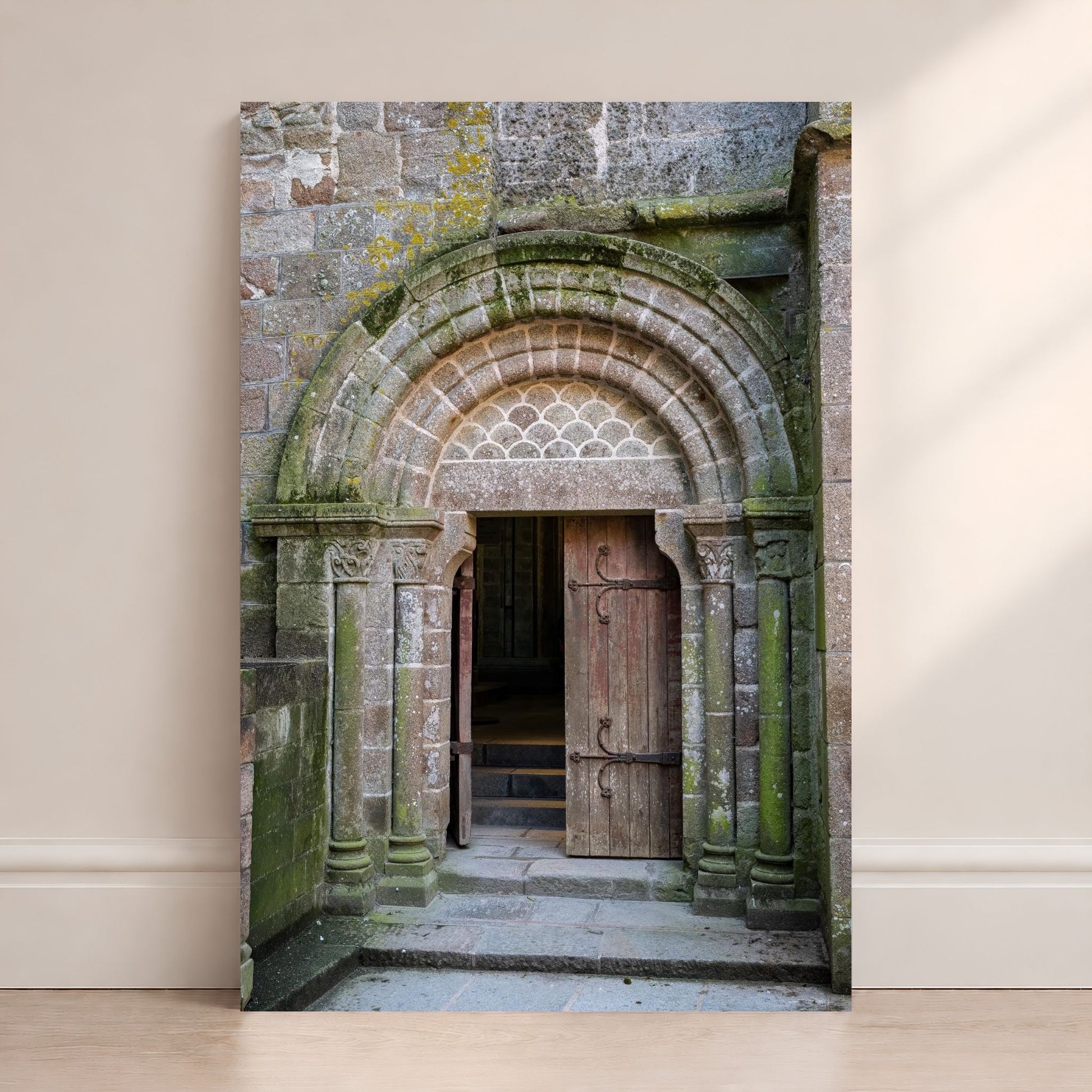 Mont Saint-Michel Abbey doorway photography print leaning against a wall, featuring an ancient stone arch and wooden door