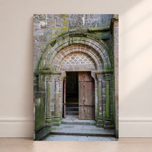 Mont Saint-Michel Abbey doorway photography print leaning against a wall, featuring an ancient stone arch and wooden door