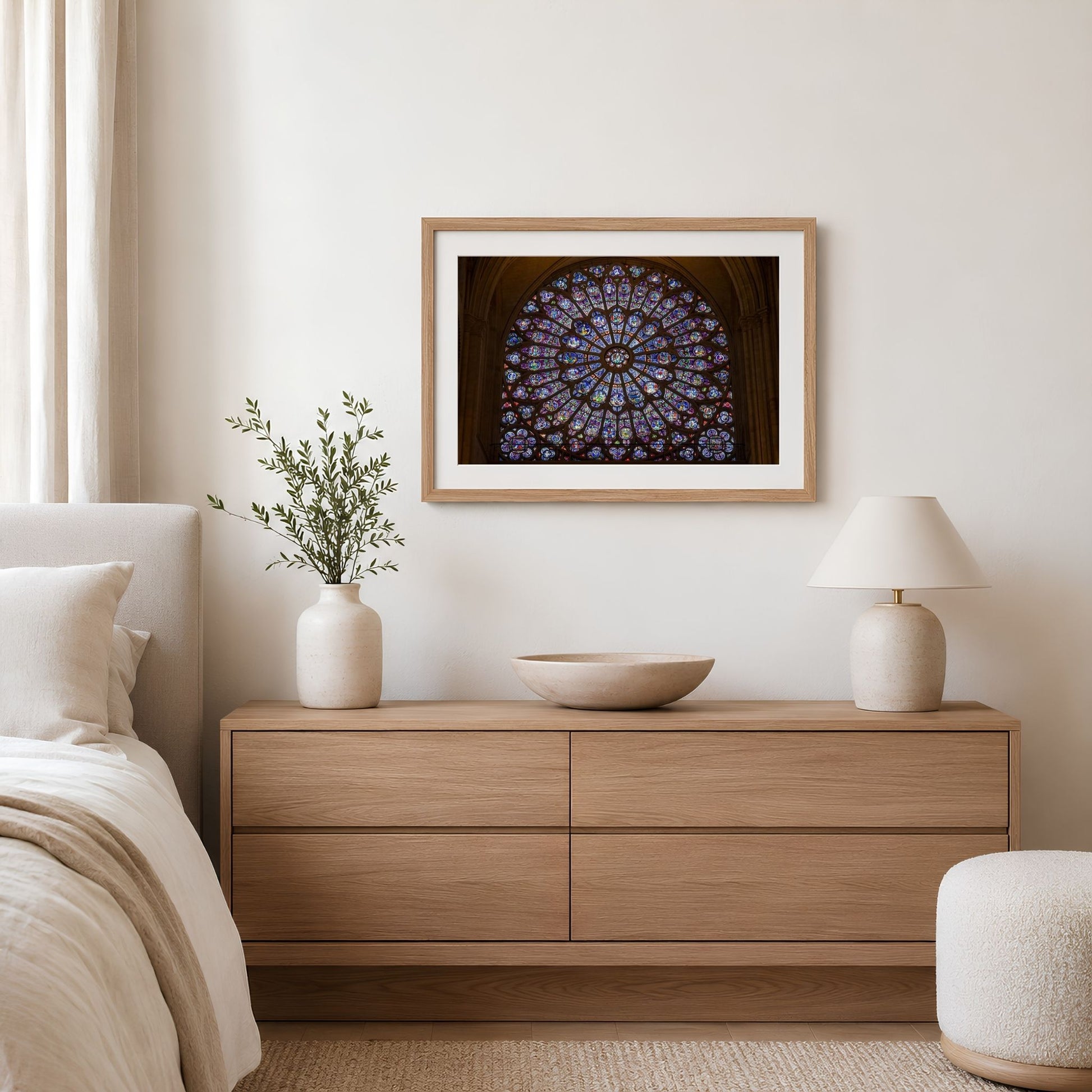 Framed Notre-Dame rose window photography print displayed above a wood dresser in a bright neutral bedroom