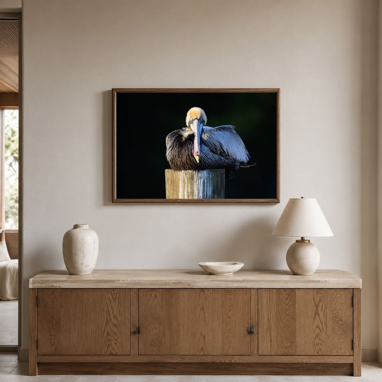 Framed artwork of a pelican on a wall above a wooden cabinet with decorative items.
