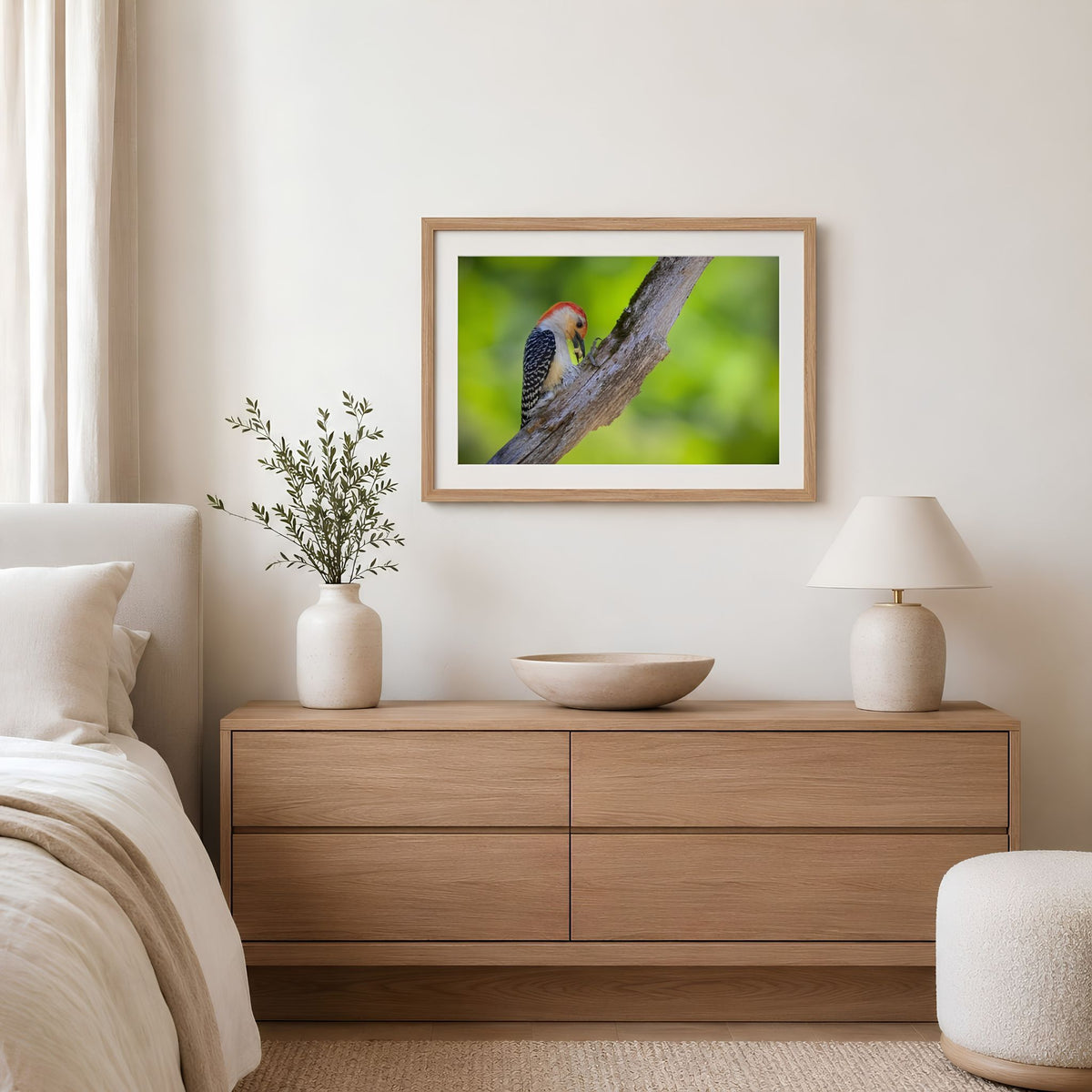 Framed picture of a bird on a branch above a wooden dresser in a bedroom.