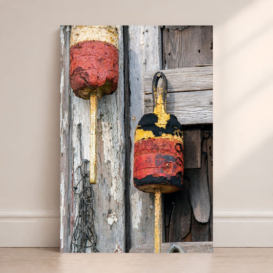 Weathered red, yellow, black, and white lobster buoys hanging on rustic wooden boards with peeling paint and coastal texture