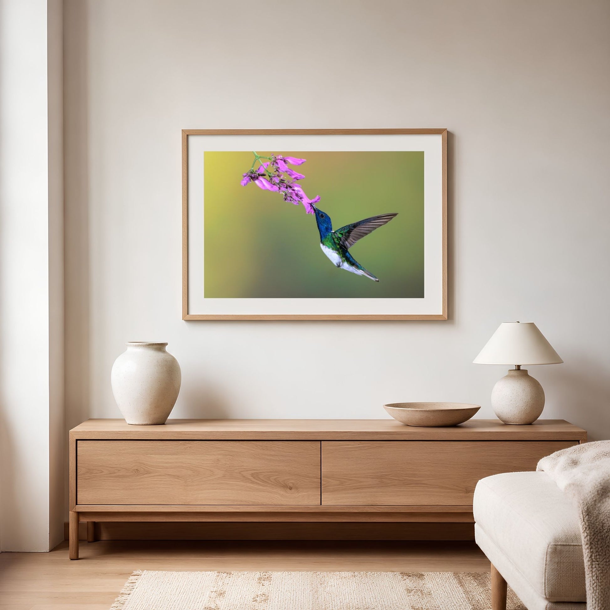 Framed artwork of a hummingbird and flower above a wooden console table in a living room.