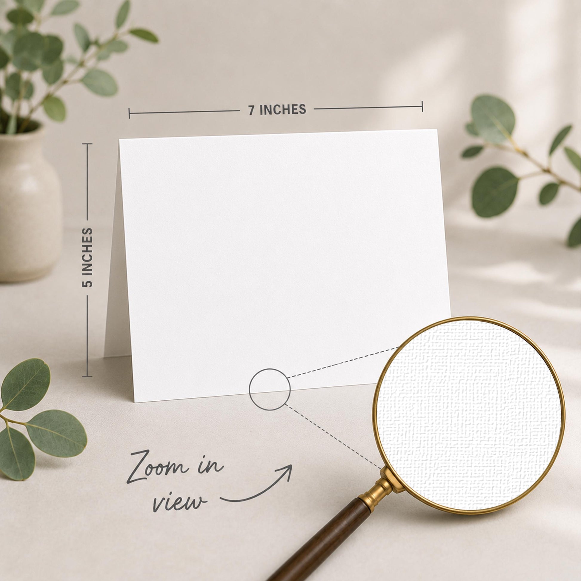 a blank white card placed on a table, with a magnifying glass nearby. The card is 5 inches wide and 7 inches tall, as indicated by the text "5 INCHES" and "7 INCHES" above and below the card, respectively. The magnifying glass is also shown in the image, with the text "Zoom in view" written below it.