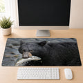 Black bear standing in a river with a freshly caught salmon in its mouth, shown as a desk mat design on a wood desk