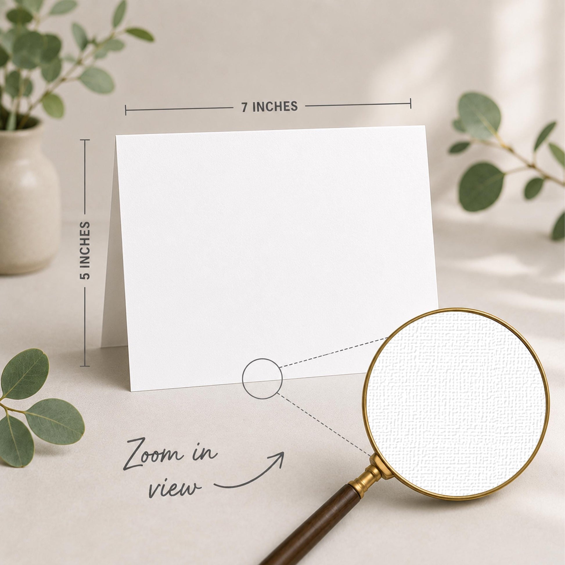 a blank white card placed on a table, with a magnifying glass nearby. The card is 5 inches wide and 7 inches tall, as indicated by the text "5 INCHES" and "7 INCHES" above and below the card, respectively. The magnifying glass is also shown in the image, with the text "Zoom in view" written below it.