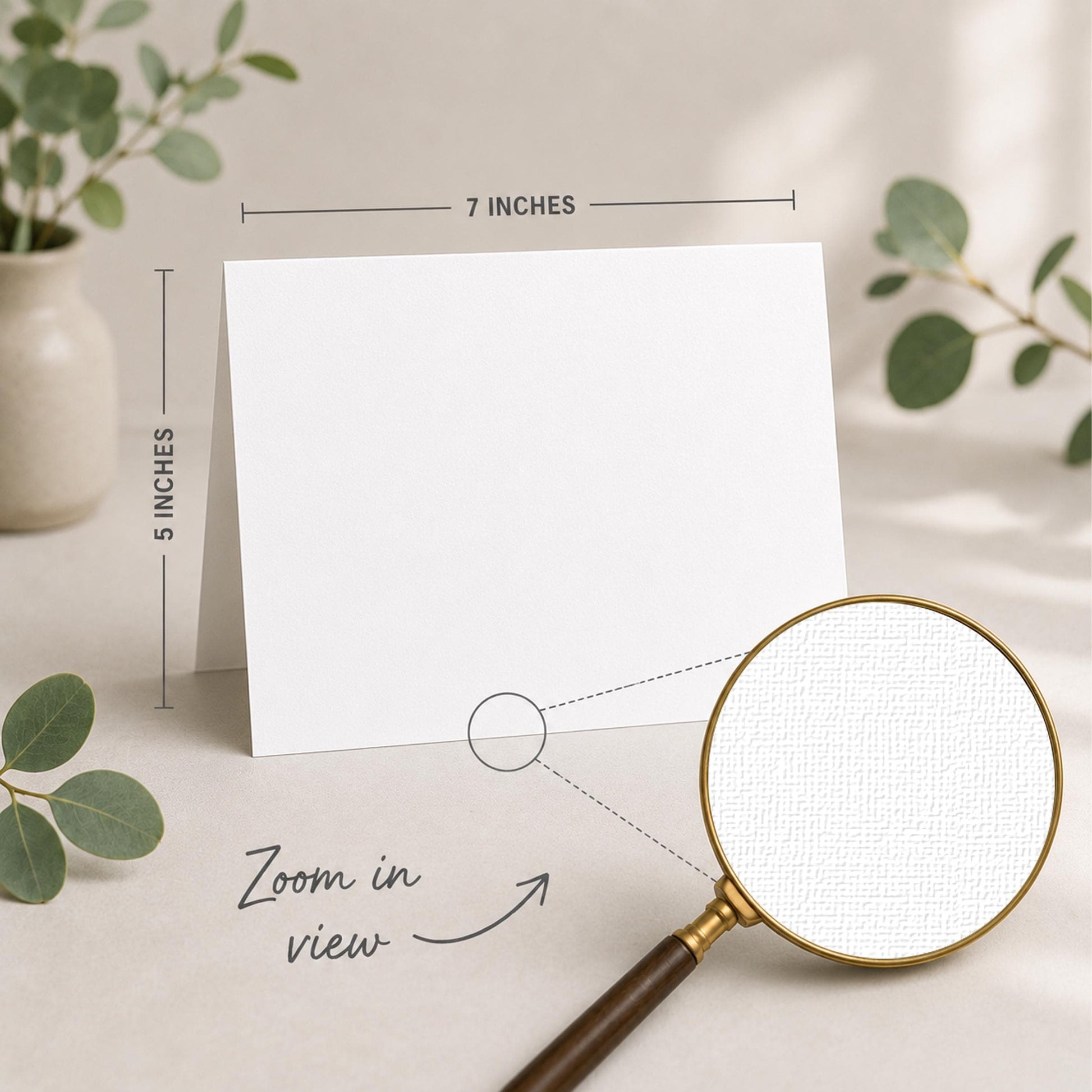 a blank white card placed on a table, with a magnifying glass nearby. The card is 5 inches wide and 7 inches tall, as indicated by the text "5 INCHES" and "7 INCHES" above and below the card, respectively. The magnifying glass is also shown in the image, with the text "Zoom in view" written below it.
