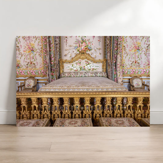an ornate, gilded bed with floral patterns and a white headboard, situated in a room with a white wall and wooden floor.