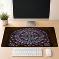 Notre-Dame Cathedral's circular stained glass rose window in jewel-toned blue, red, and gold, shown as a desk mat design on a wood desk