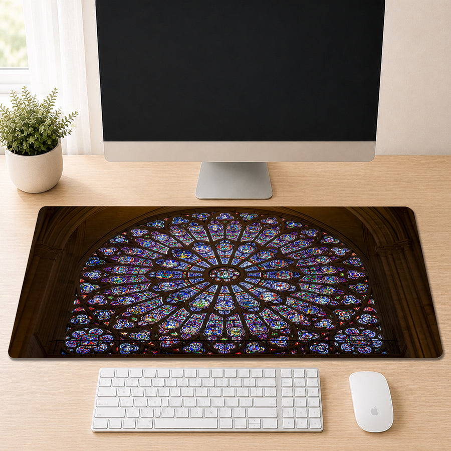 Notre-Dame Cathedral's circular stained glass rose window in jewel-toned blue, red, and gold, shown as a desk mat design on a wood desk