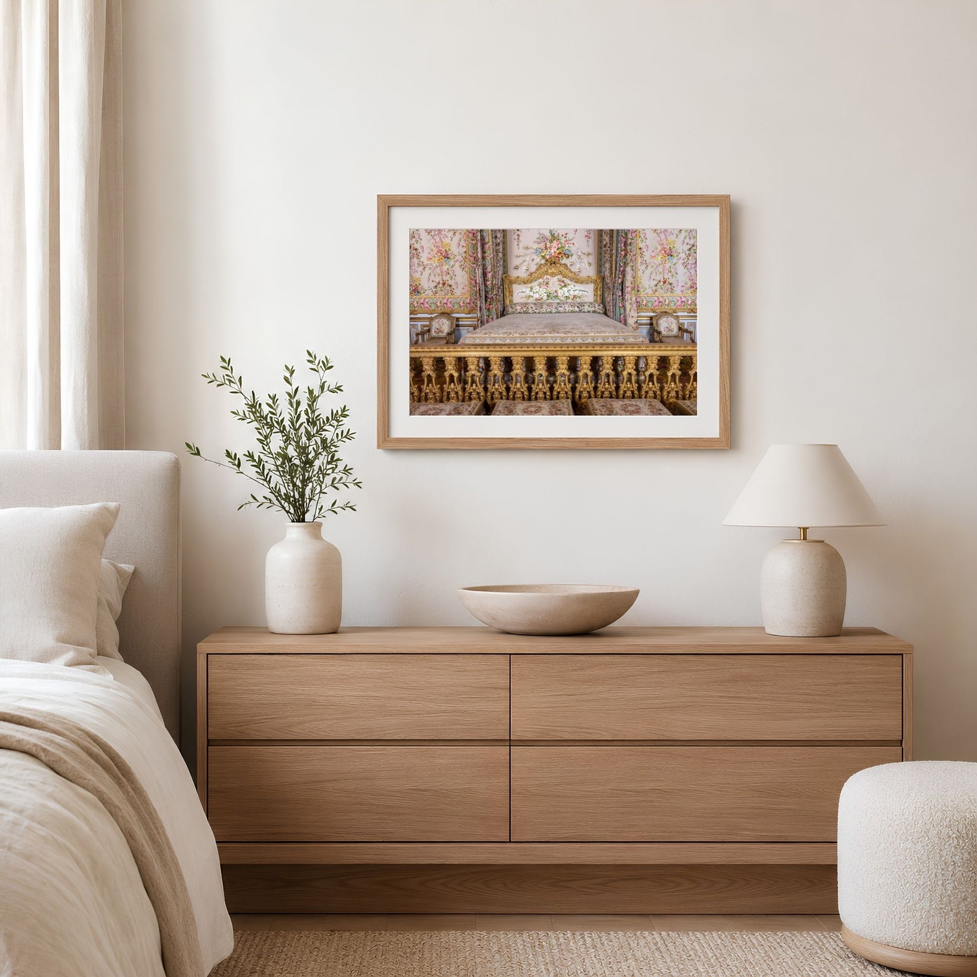 a serene and elegant bedroom setting, featuring a wooden dresser with a bowl on top, a framed picture of a palace, a lamp, and a plant.
