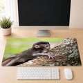 Baby macaque climbing a mossy tree branch with an outstretched hand, shown as a desk mat design on a wood desk