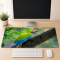 Great Green Macaw perched on a tree branch with green plumage and a red forehead patch, shown as a desk mat design on a wood desk