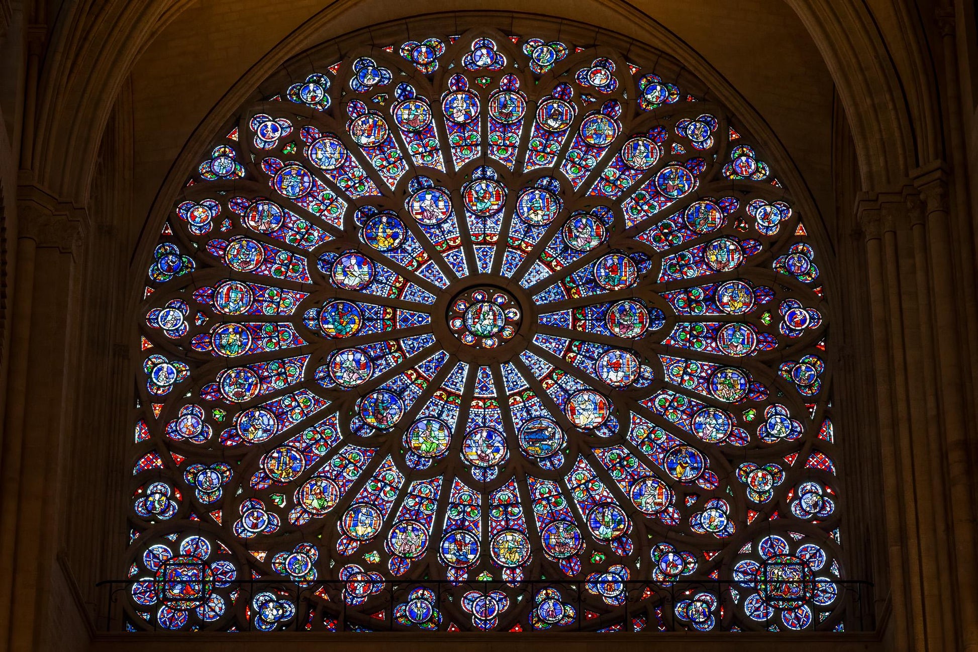 Colorful rose window inside Notre-Dame de Paris, framed by dark Gothic stone arches and glowing stained glass panels in red, blue, green, and gold.