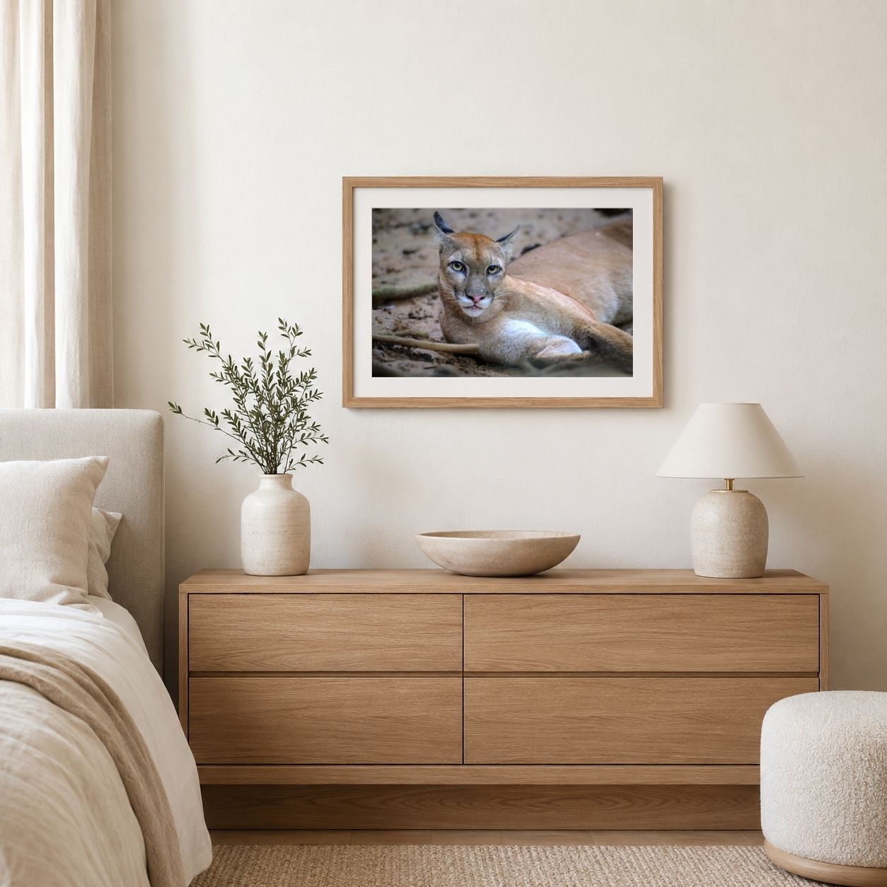 Framed picture of a cougar on a wall above a wooden dresser in a bedroom.